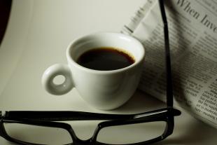Glasses and a cup of coffee resting next to a newspaper on a white table