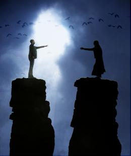 Two people standing on tall peaks reaching out to each other across the chasm