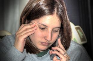 A woman talks on the phone, rubbing her temple and feeling stressed